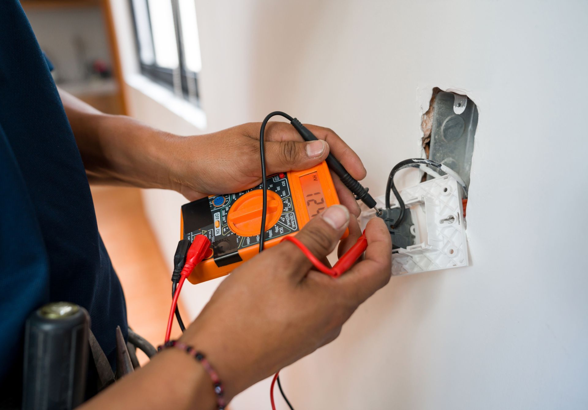 A person is using a multimeter to test a light switch.