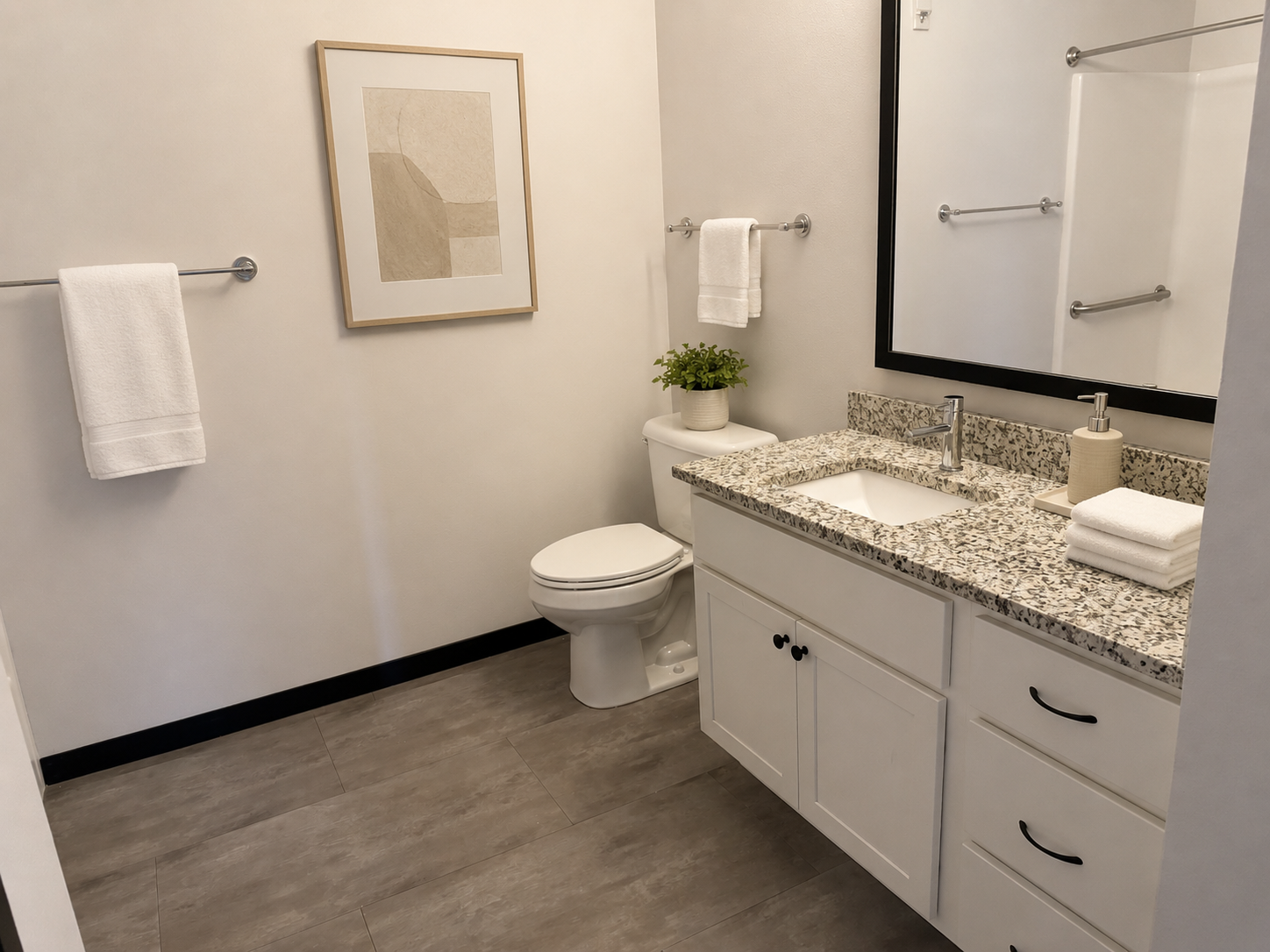 Modern bathroom with granite vanity, toilet, towel racks, wall art, and large mirror