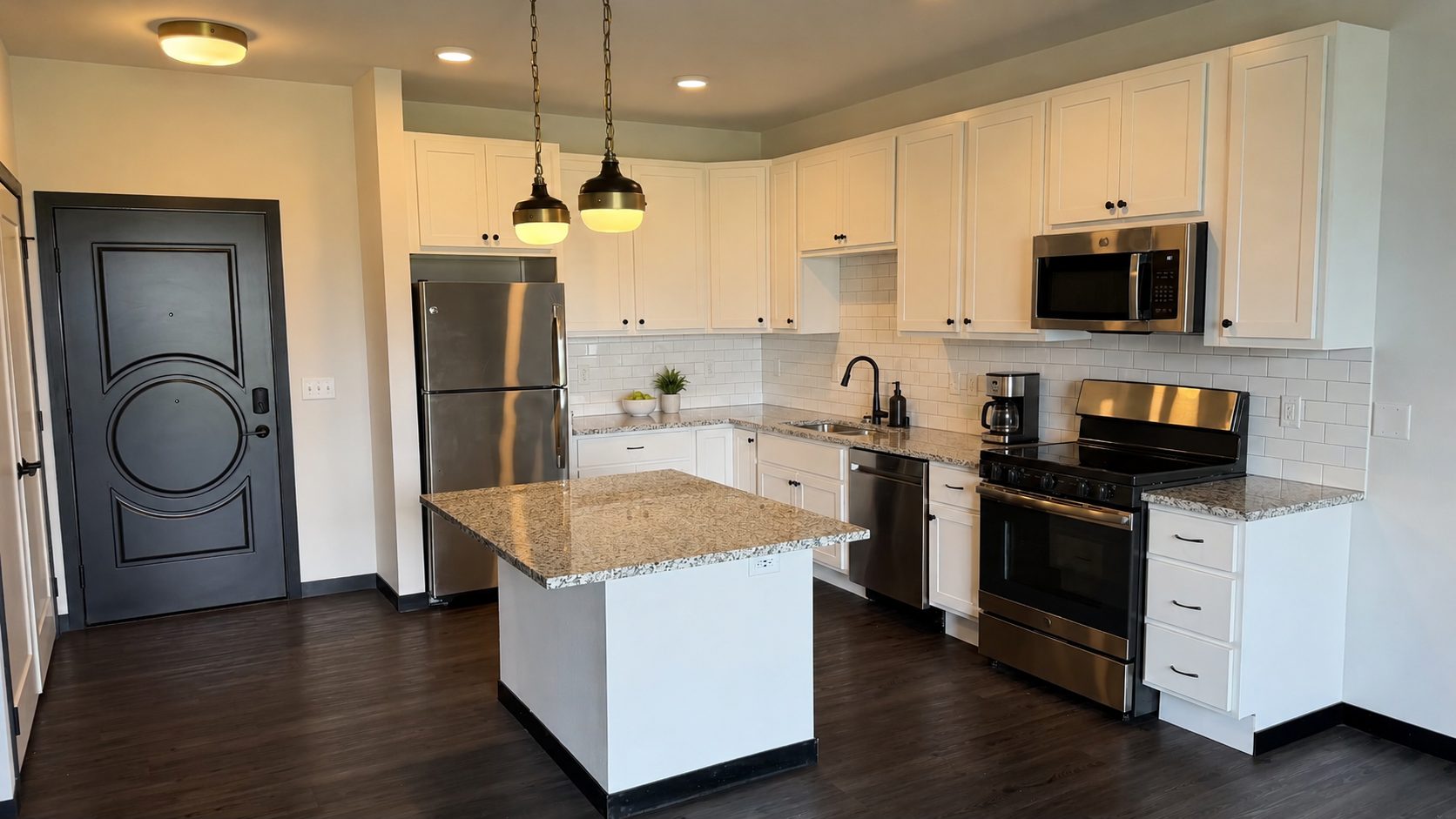 Modern white kitchen with granite island, stainless appliances, dark floors, and gray front door