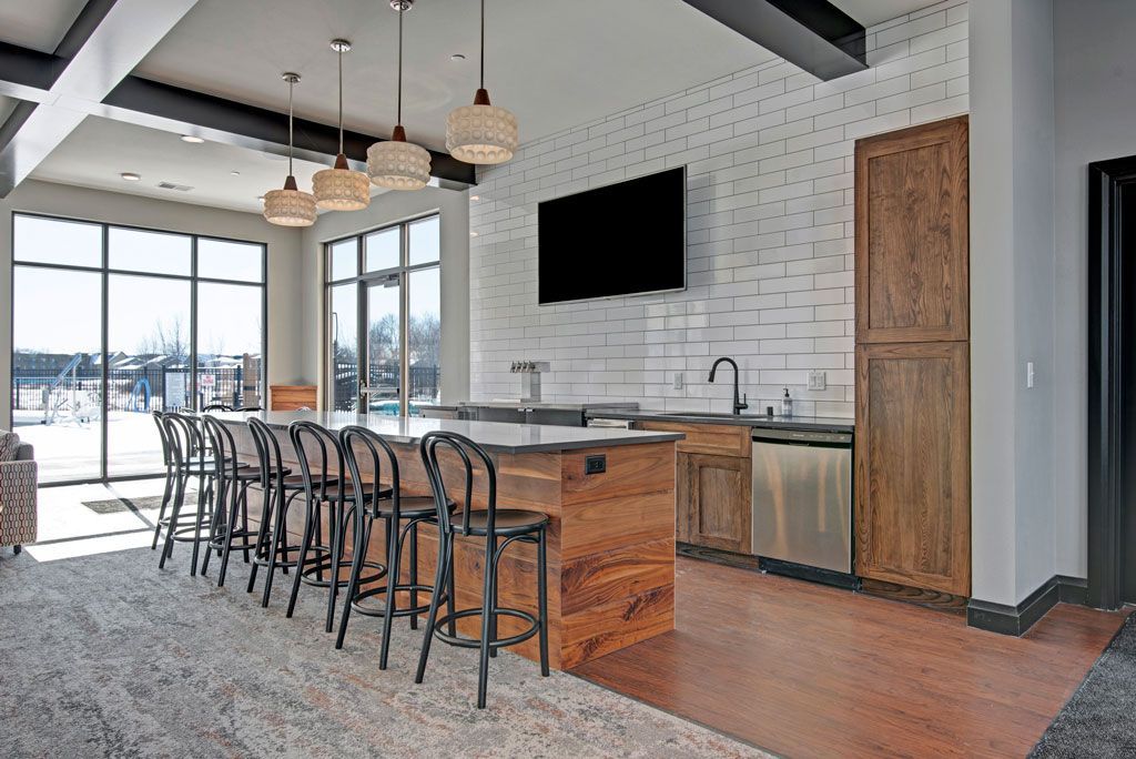 Modern kitchen with island seating, wood accents, pendant lights, and large windows overlooking a balcony
