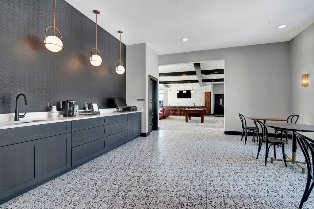 Modern kitchen with dark cabinets, pendant lights, speckled floor, and a small seating area.