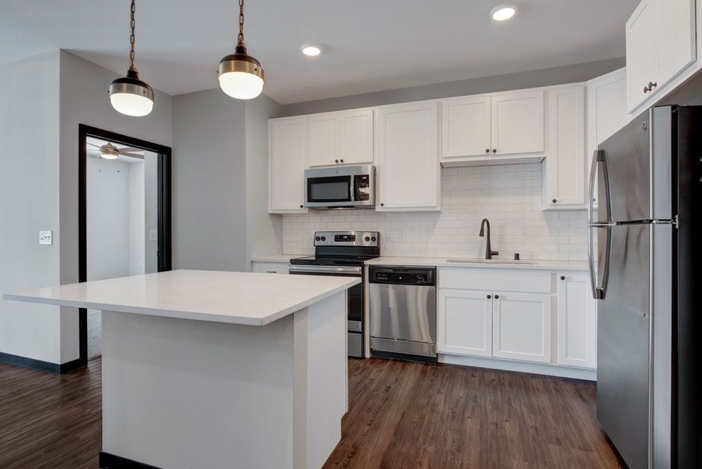 Bright modern kitchen with white cabinets, stainless appliances, island, and dark wood floors