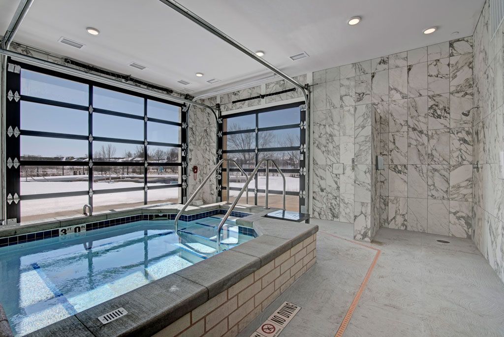 Indoor pool room with large windows, tiled walls, and a raised spa or hot tub.