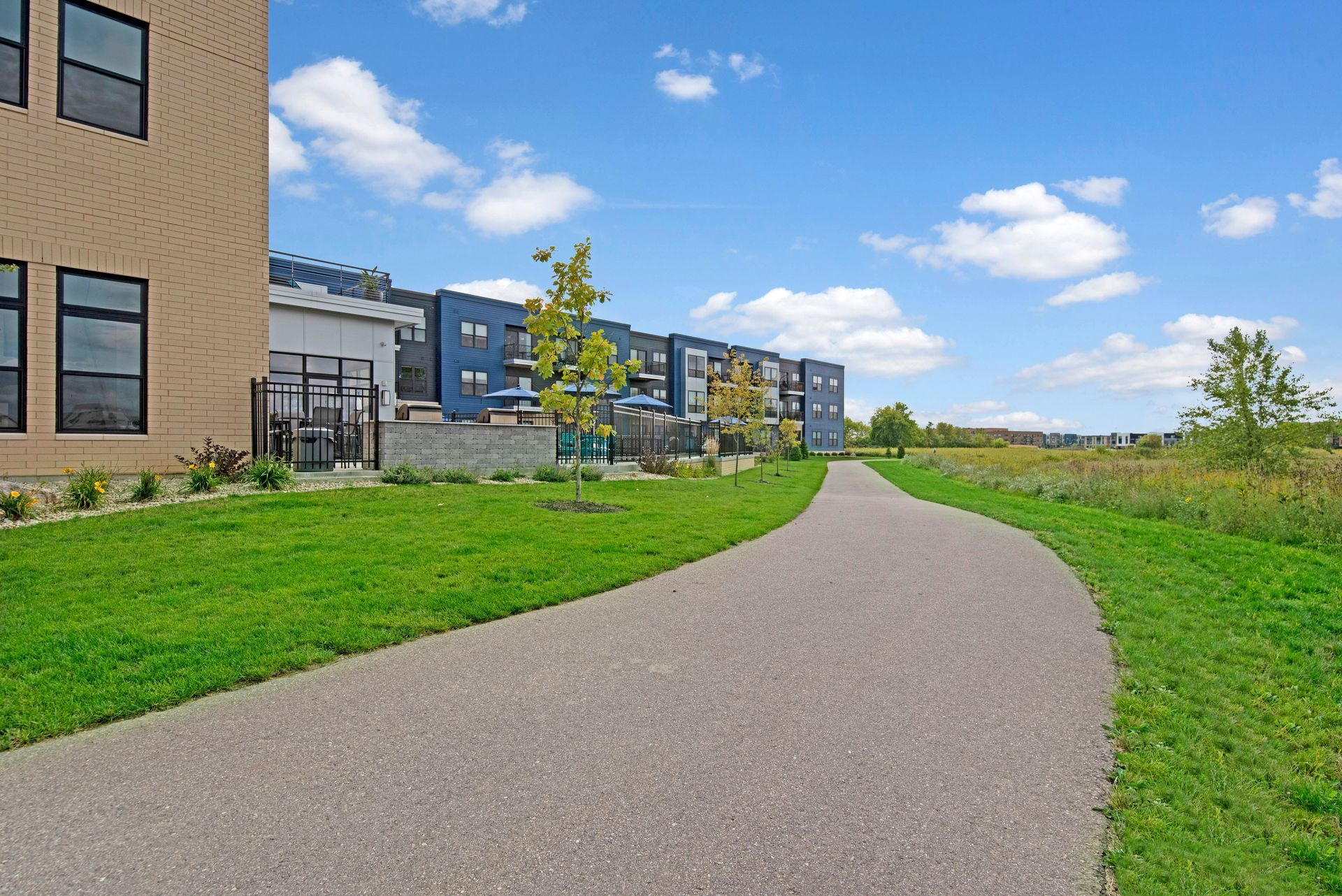Curved path beside modern apartment buildings and green lawn under a blue sky with clouds