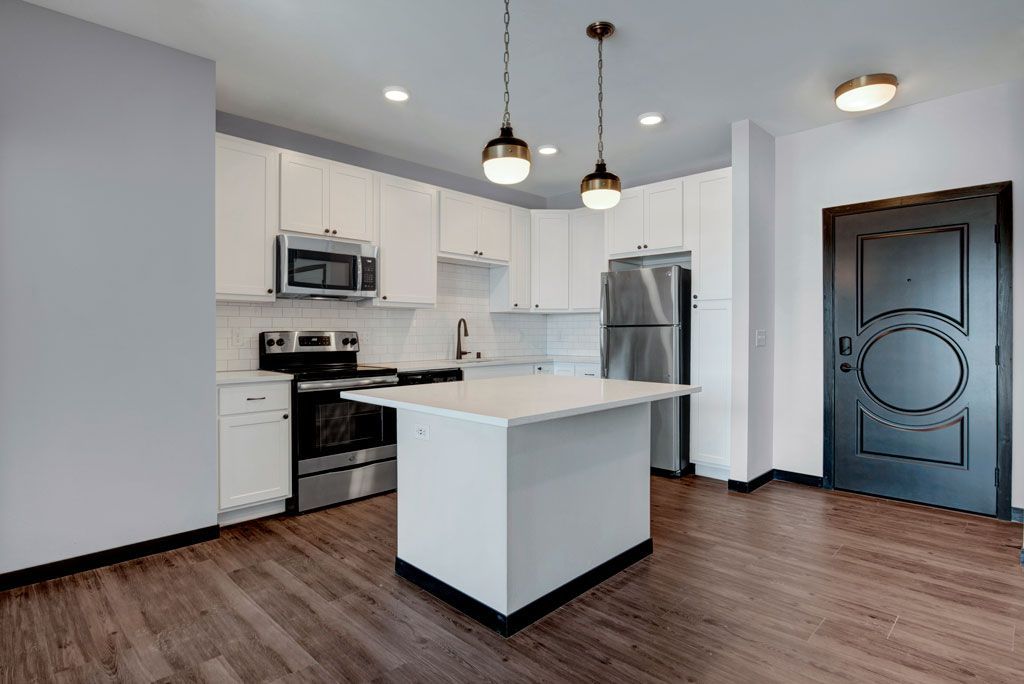 Modern kitchen with white cabinets, island, stainless steel appliances, pendant lights, and dark wood floor