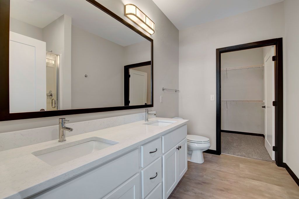 Modern bathroom with double vanity, large mirror, and open doorway to adjoining room.