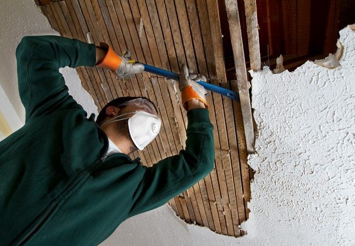 Worker using crowbar to remove plaster ceiling lathe