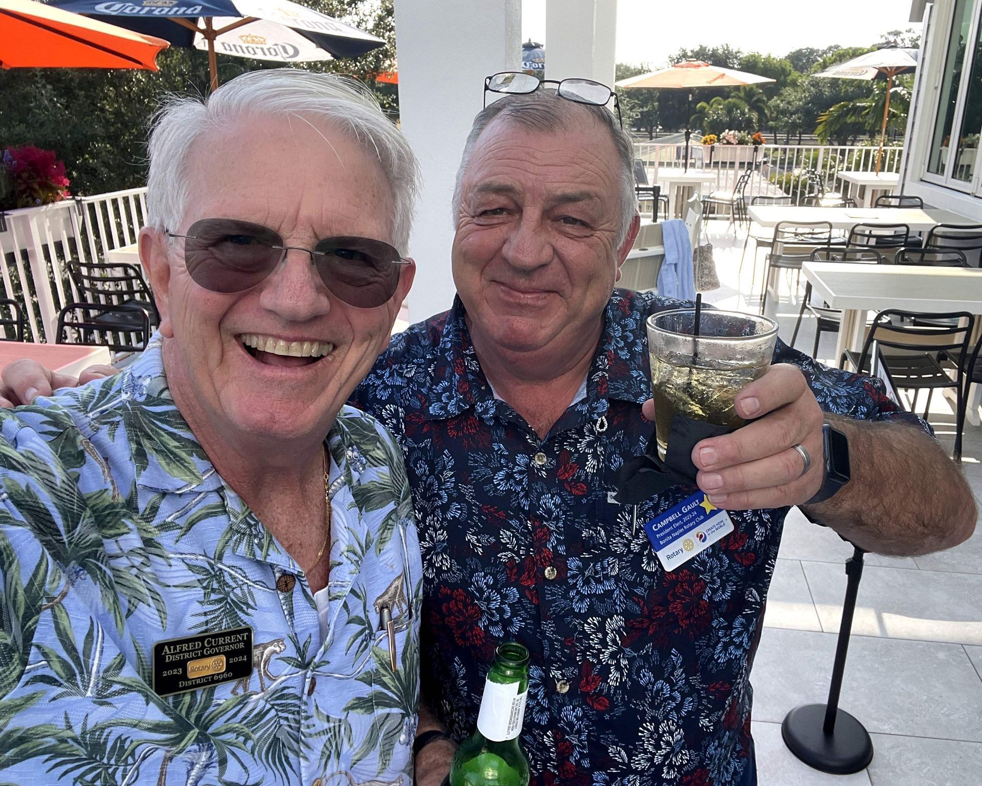 Two men are standing next to each other holding drinks and smiling.