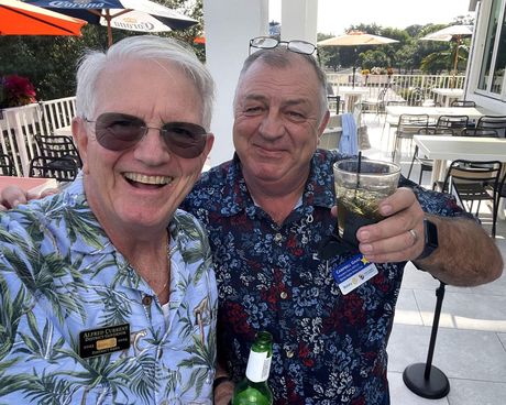 Two men are standing next to each other holding drinks and smiling.
