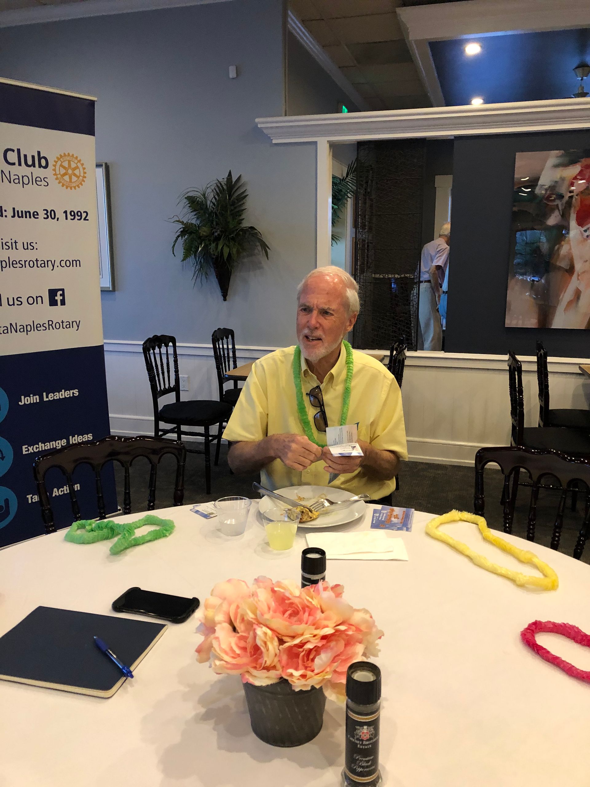 A man in a yellow shirt is sitting at a table with flowers in a vase.