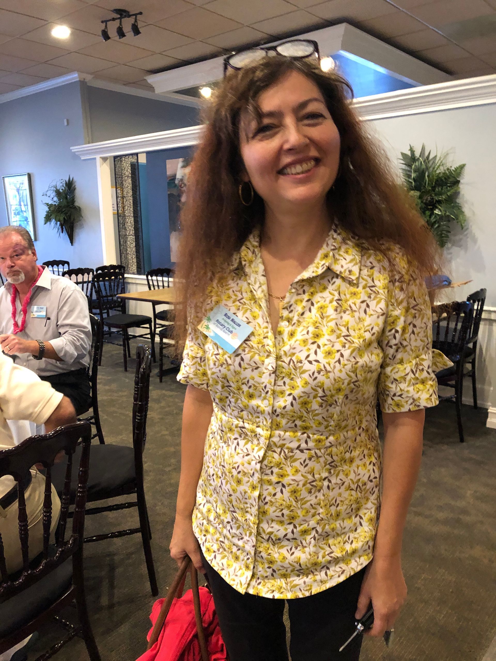 A woman in a yellow shirt is smiling in a restaurant while holding a red bag.