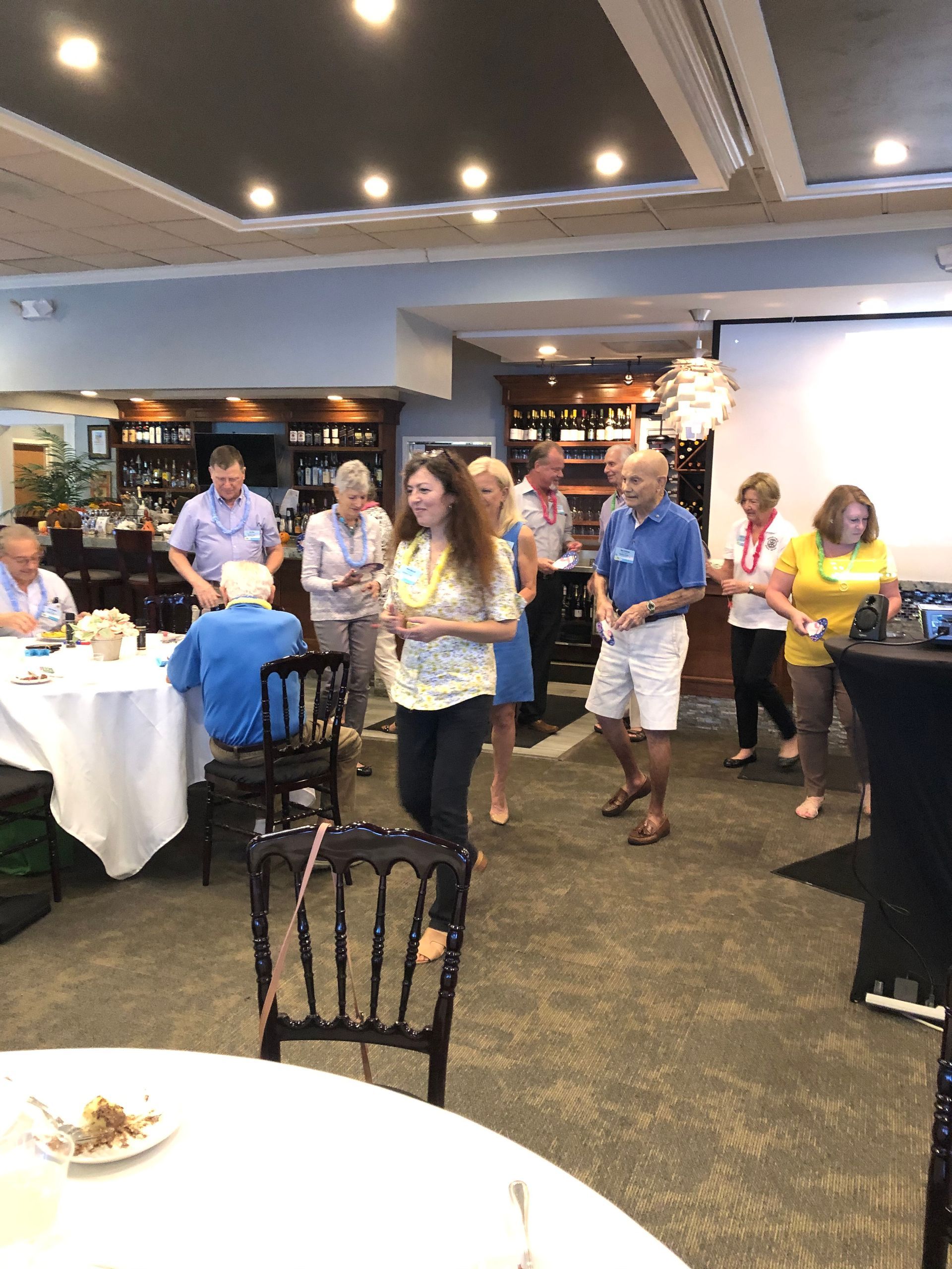 A group of people are dancing in a room with tables and chairs.