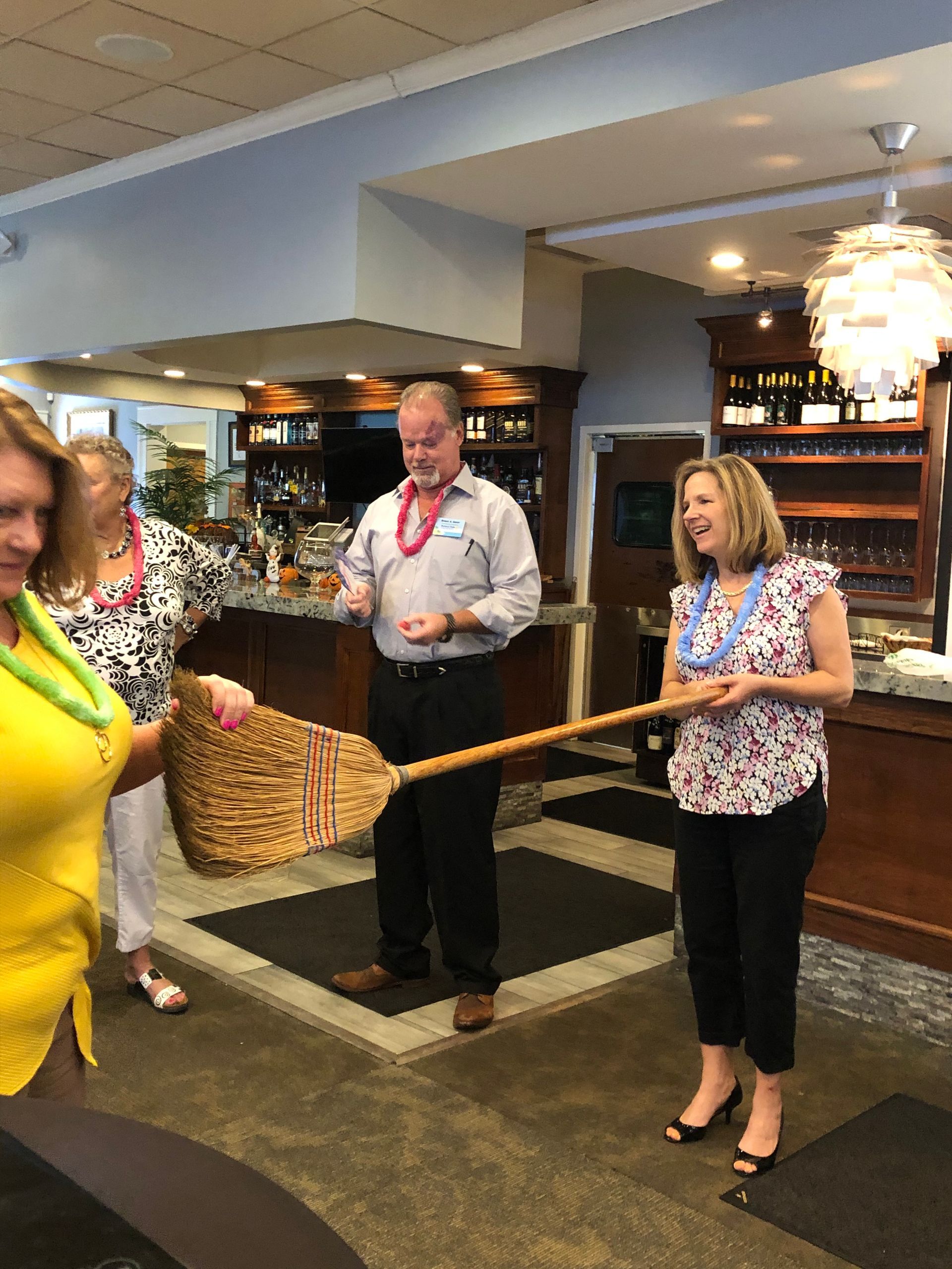 A group of people are standing in a room holding a broom.