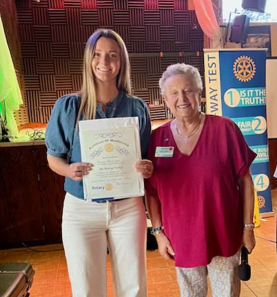 Woman holding a certificate next to another woman, indoors. Both are smiling.