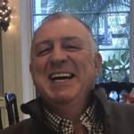 A man is smiling with his eyes closed in front of a window.