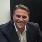Man with short brown hair wearing a suit and smiling.