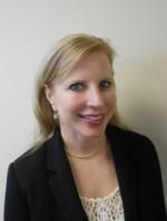 A woman in a black jacket and white top is smiling for the camera.