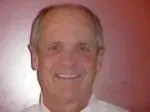 Smiling man, fair skin, thinning hair, white shirt, red background.