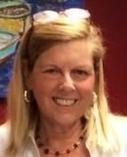 A woman wearing sunglasses and a necklace is smiling in front of a painting.