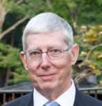 A man wearing glasses and a suit and tie is smiling for the camera.