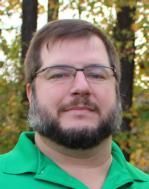 A man with a beard and glasses is wearing a green shirt.