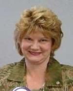 A woman in a green jacket is smiling for the camera.