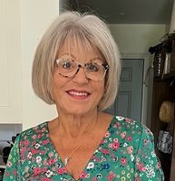 A woman wearing glasses and a green floral shirt is smiling.