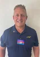 A man wearing a blue shirt and a name tag is smiling for the camera.