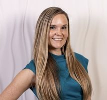 A woman with long blonde hair is wearing a blue shirt and smiling.