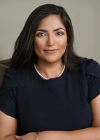 A woman in a blue shirt and pearl necklace is sitting on a couch with her arms crossed.