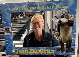 A woman is holding a picture frame with an otter mascot in it.