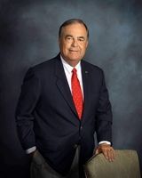 A man in a suit and tie is leaning on a chair.