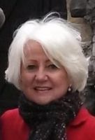 A woman with white hair is wearing a red jacket and a black scarf.
