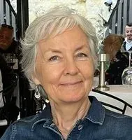 Woman with short gray hair smiling, wearing a denim shirt, seated outside.