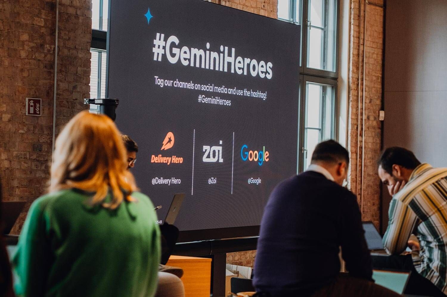 People at event with screen displaying #GeminiHeroes, featuring logos of Substack, 20i, and Google.