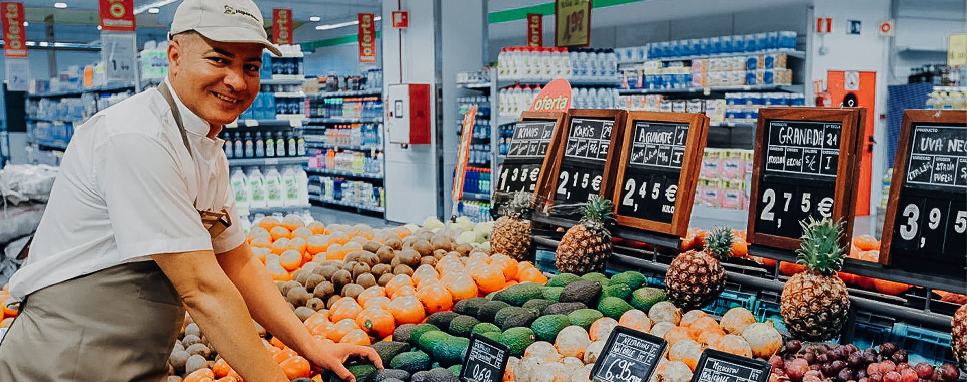 A man is standing in front of a display of fruits and vegetables in a grocery store.