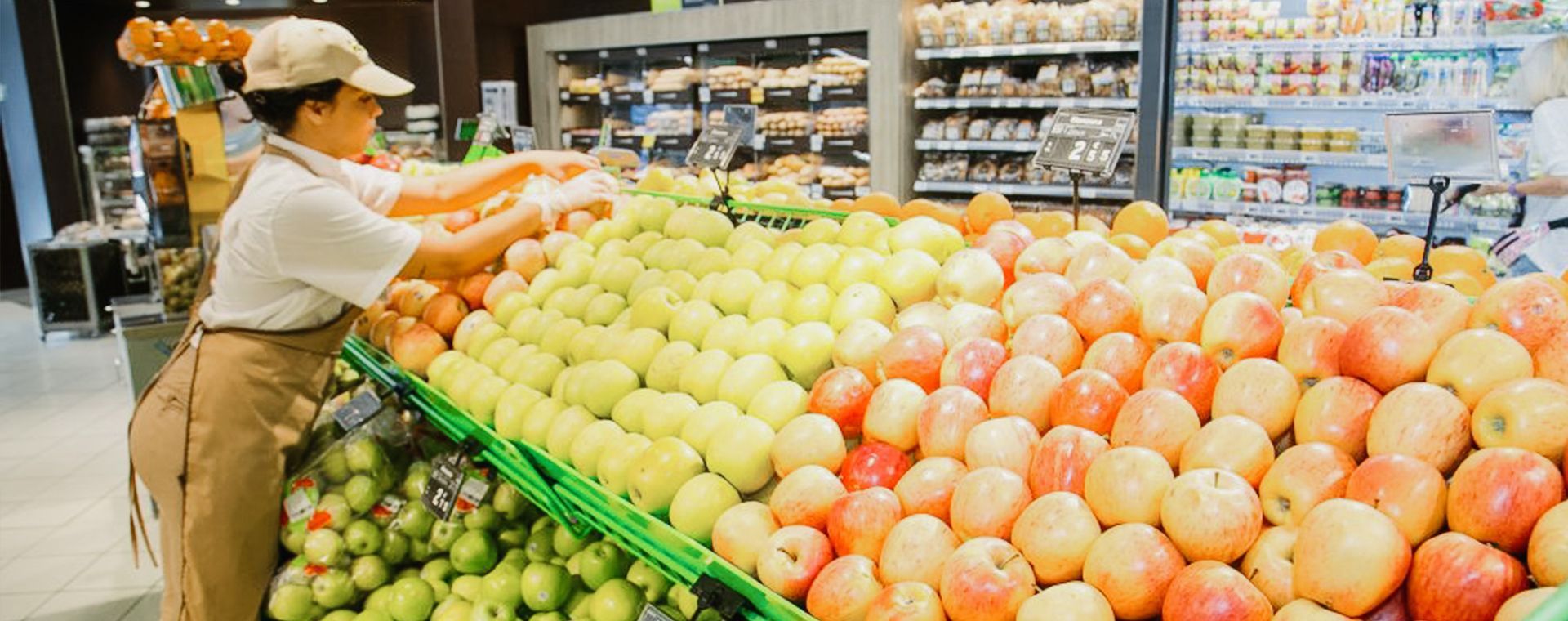 Una mujer está parada frente a una exhibición de manzanas en una tienda de comestibles.