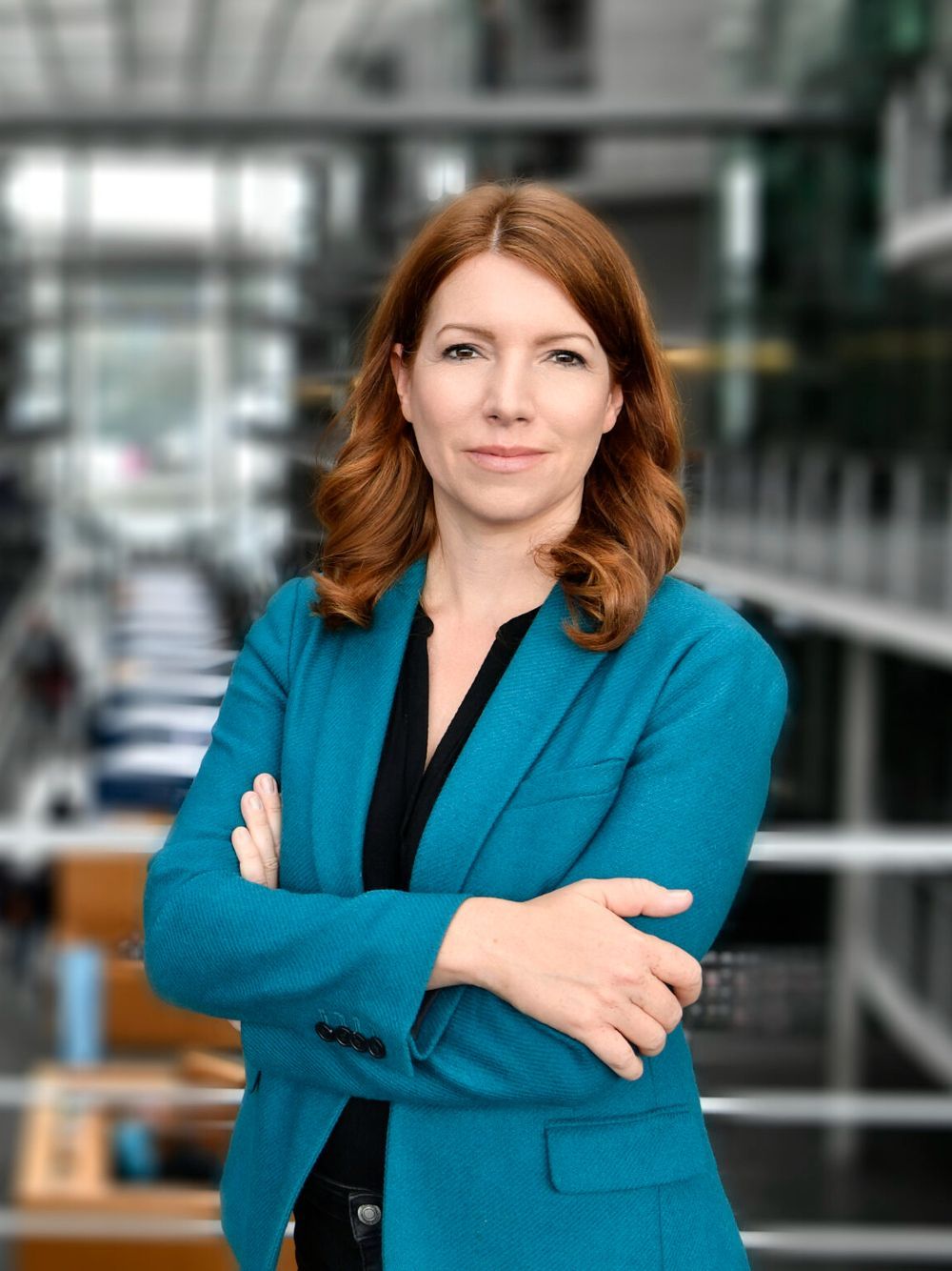 A woman in a blue jacket is standing with her arms crossed.