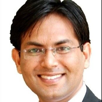Man with a beard, wearing a navy blazer and white shirt, smiling at the camera.