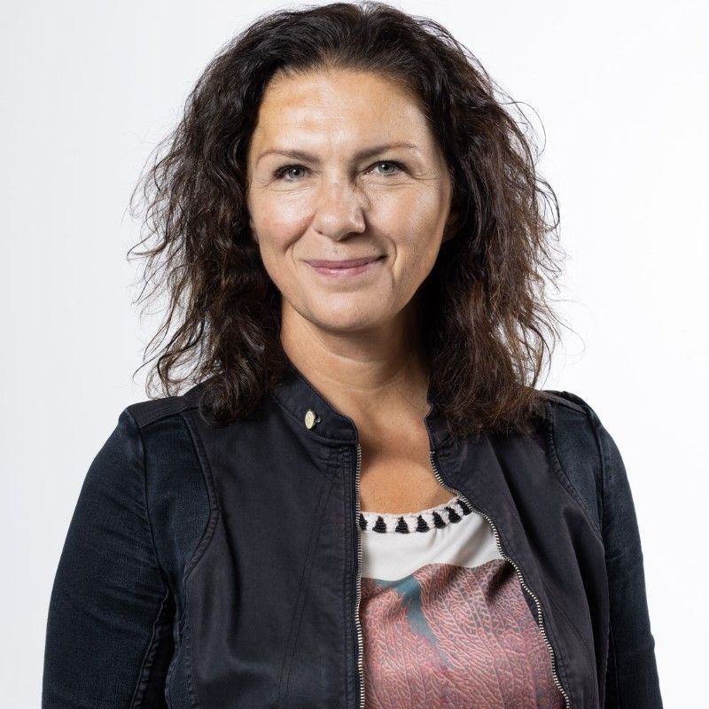 Man with a beard, wearing a navy blazer and white shirt, smiling at the camera.