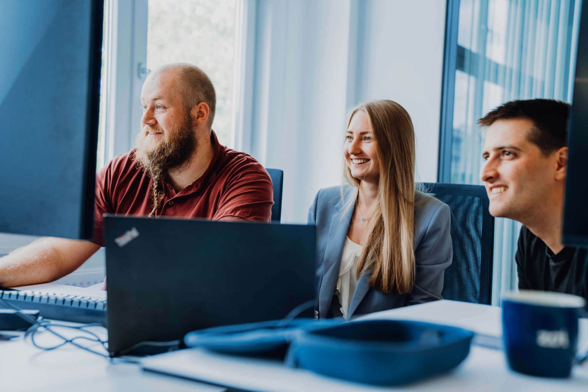 Three colleagues smiling, looking at a computer screen in a bright office.