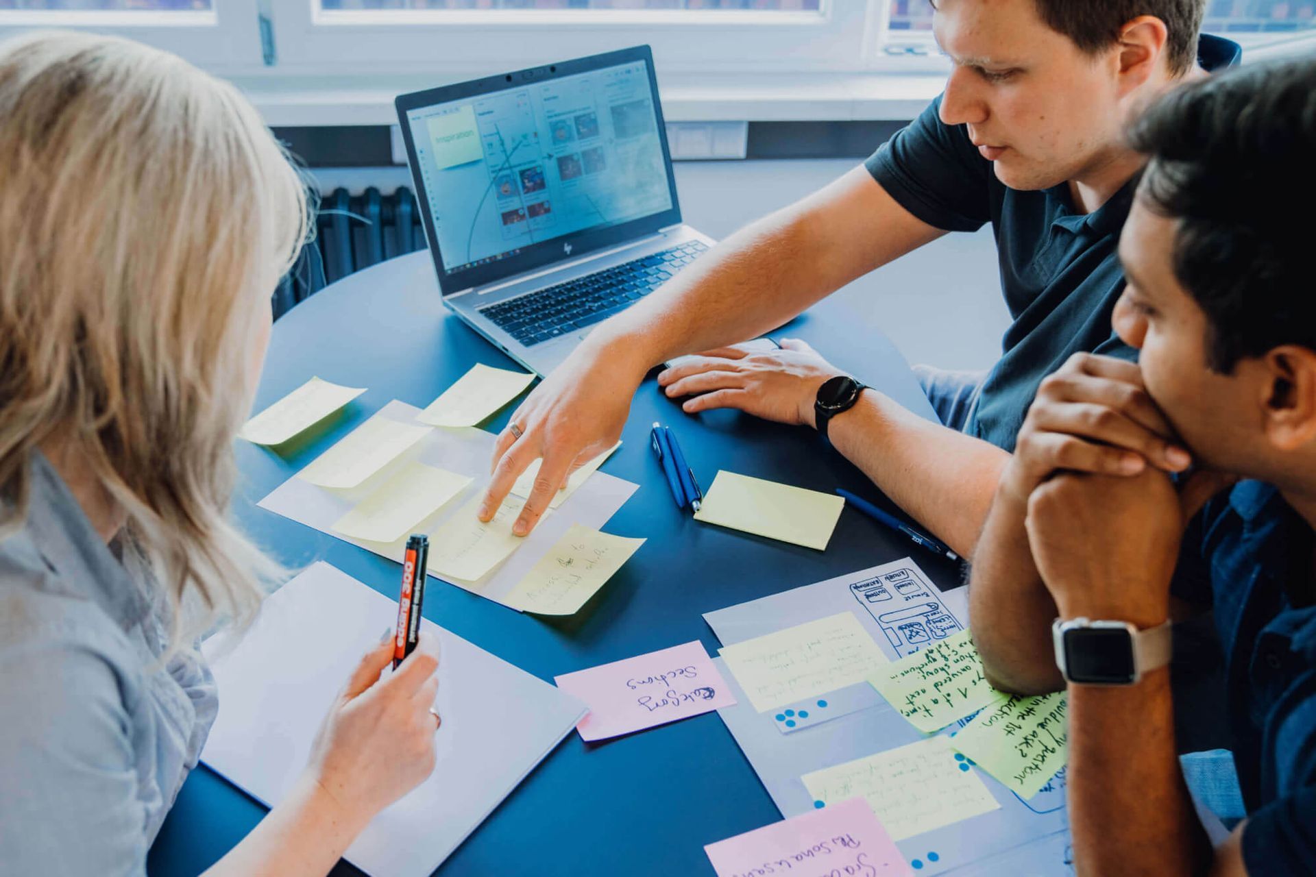 Three people collaborating around a table with sticky notes and a laptop, brainstorming ideas.