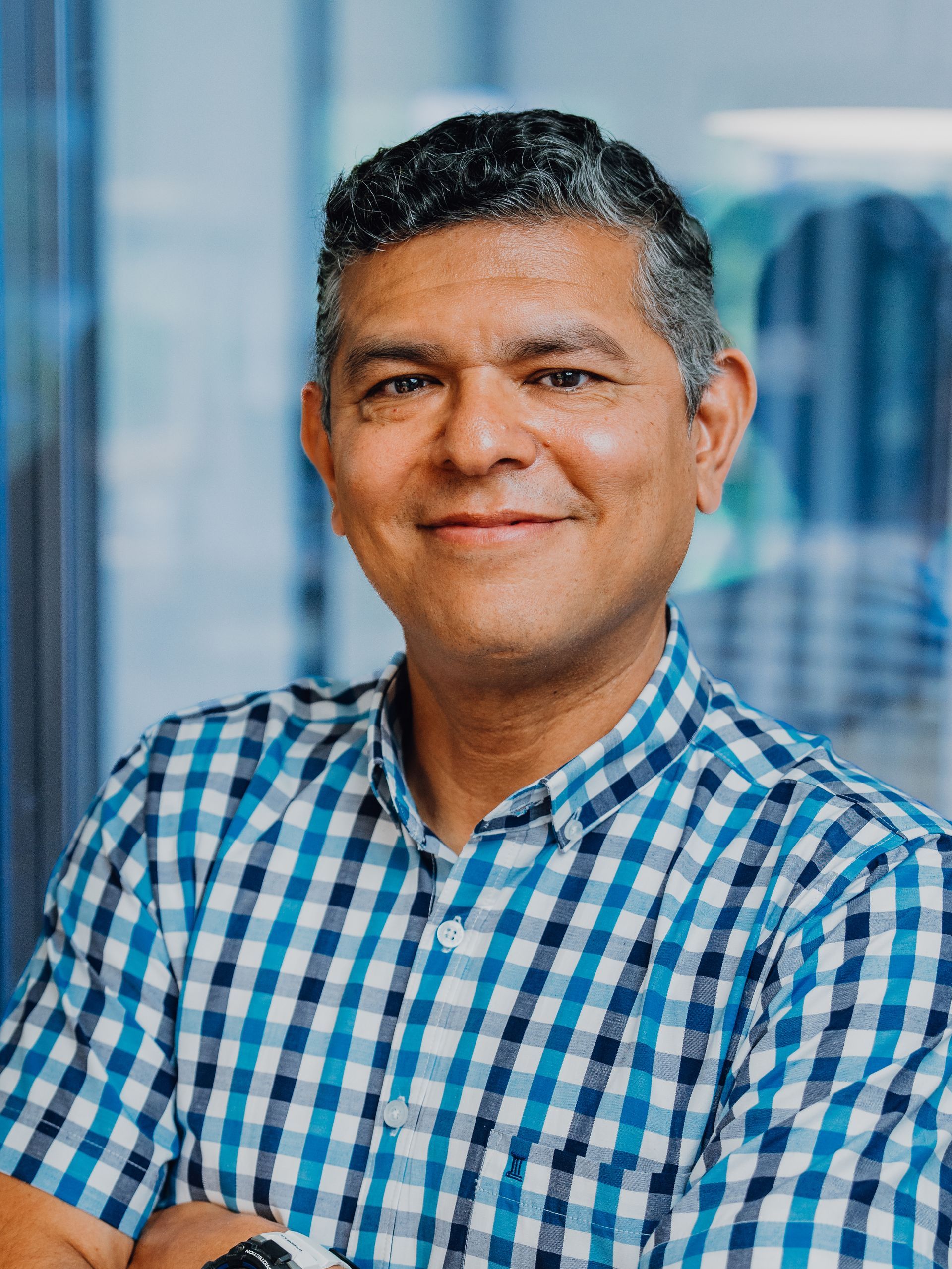 A man in a blue and white checkered shirt is smiling for the camera.