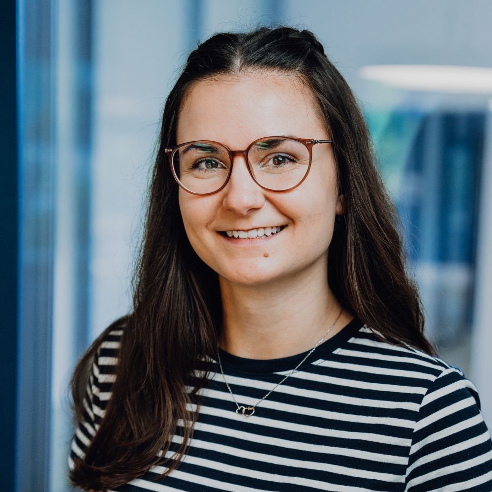 Woman with glasses smiling, wearing striped shirt, in office setting.