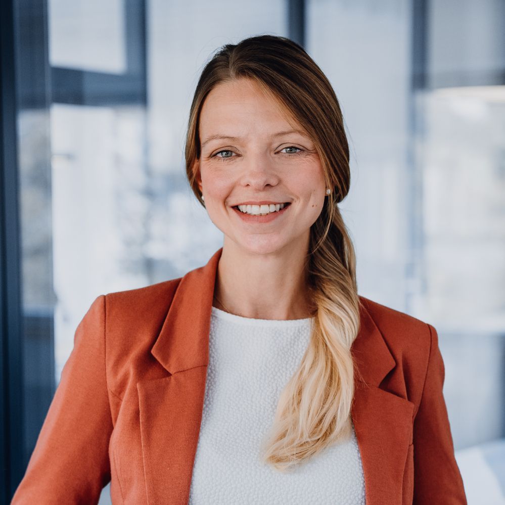 Woman in terracotta blazer smiles at the camera.