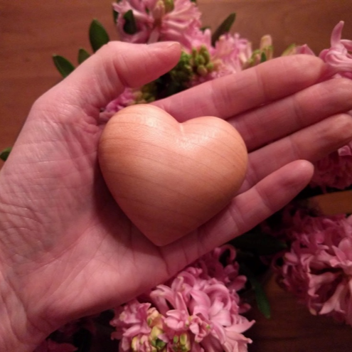 Hand met een houten hart, met roze bloemen op de achtergrond.