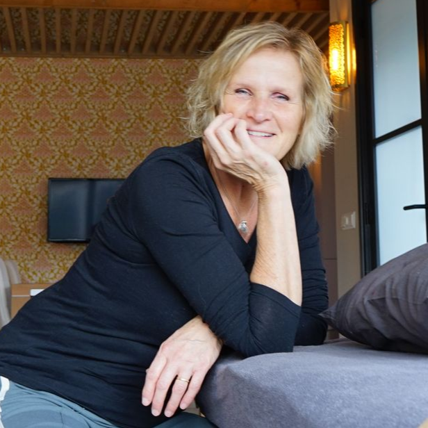 Vrouw (eigenaar Senti) met kin op haar hand, glimlachend. Leunend op de grond, binnenshuis. Zwart shirt.