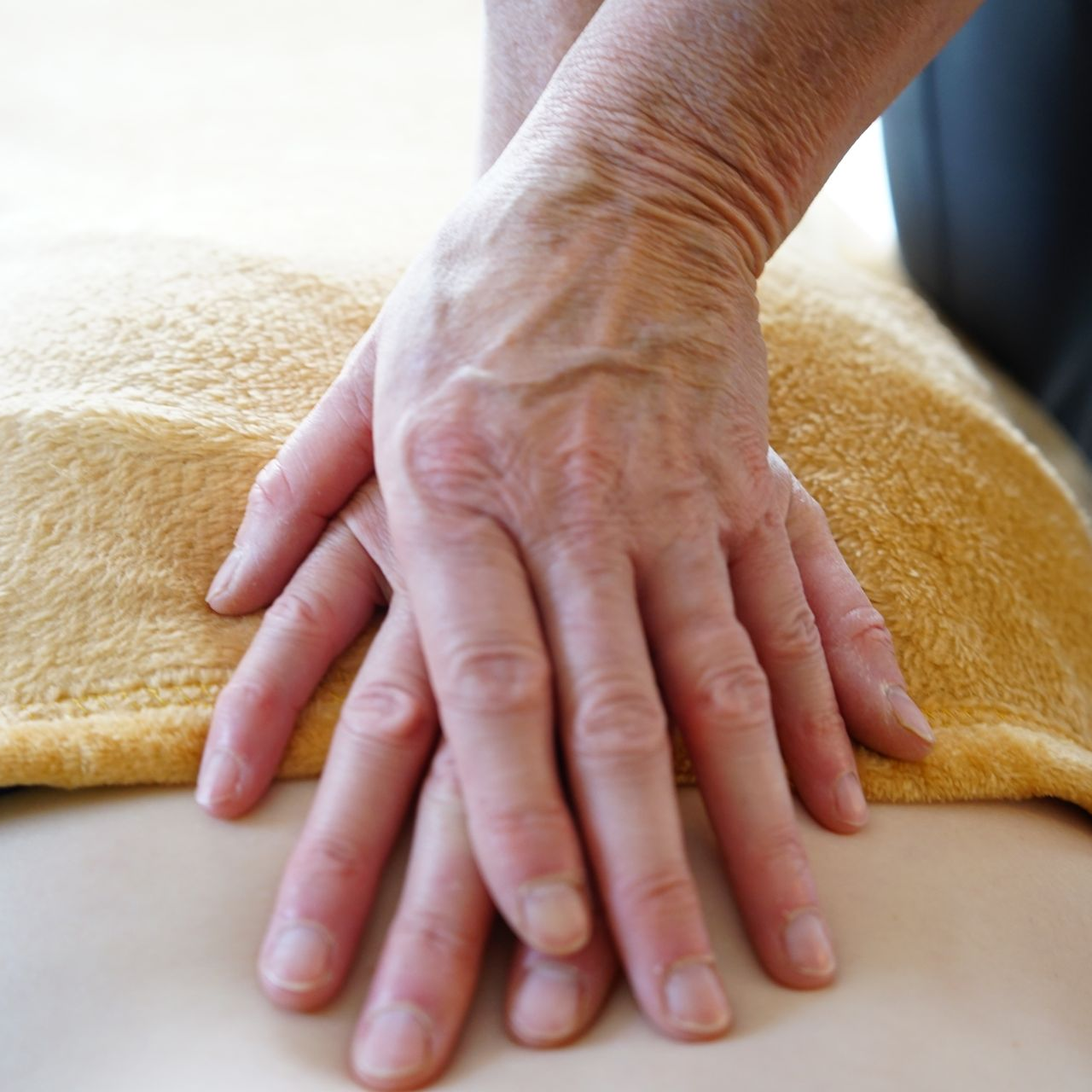 Handen rustend op de rug van een persoon, bedekt met een gele handdoek; close-up.