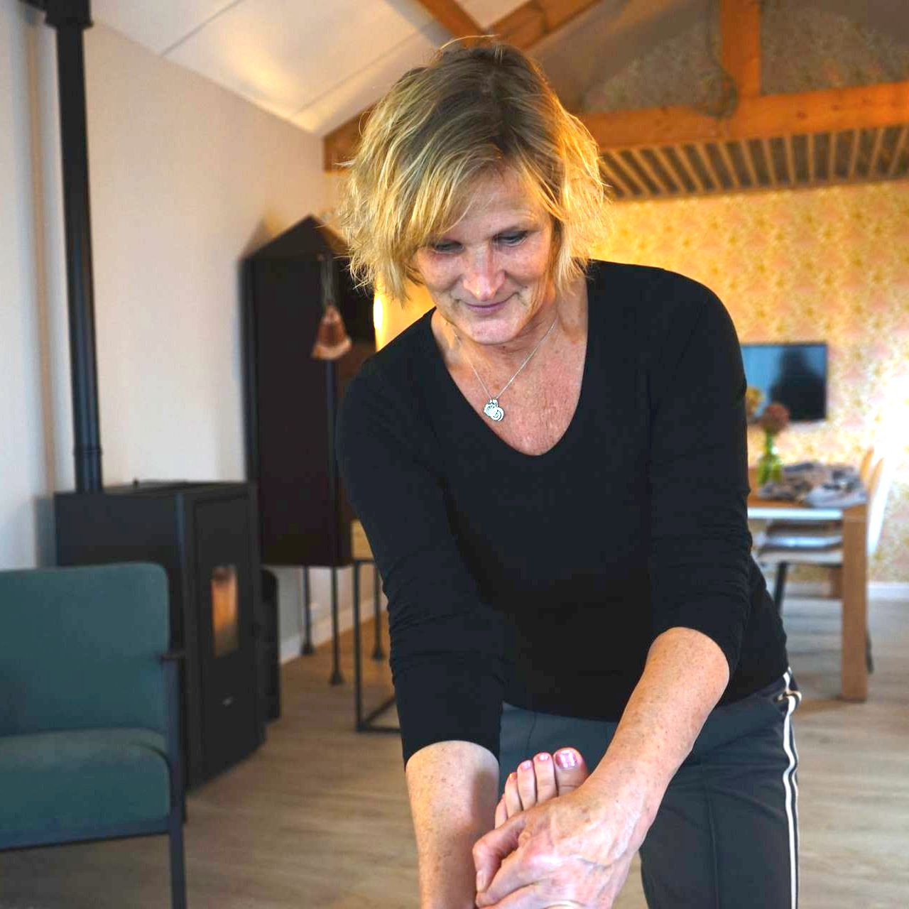 Vrouw in zwart topje masseert een voet binnenshuis; praktijkruimte.
