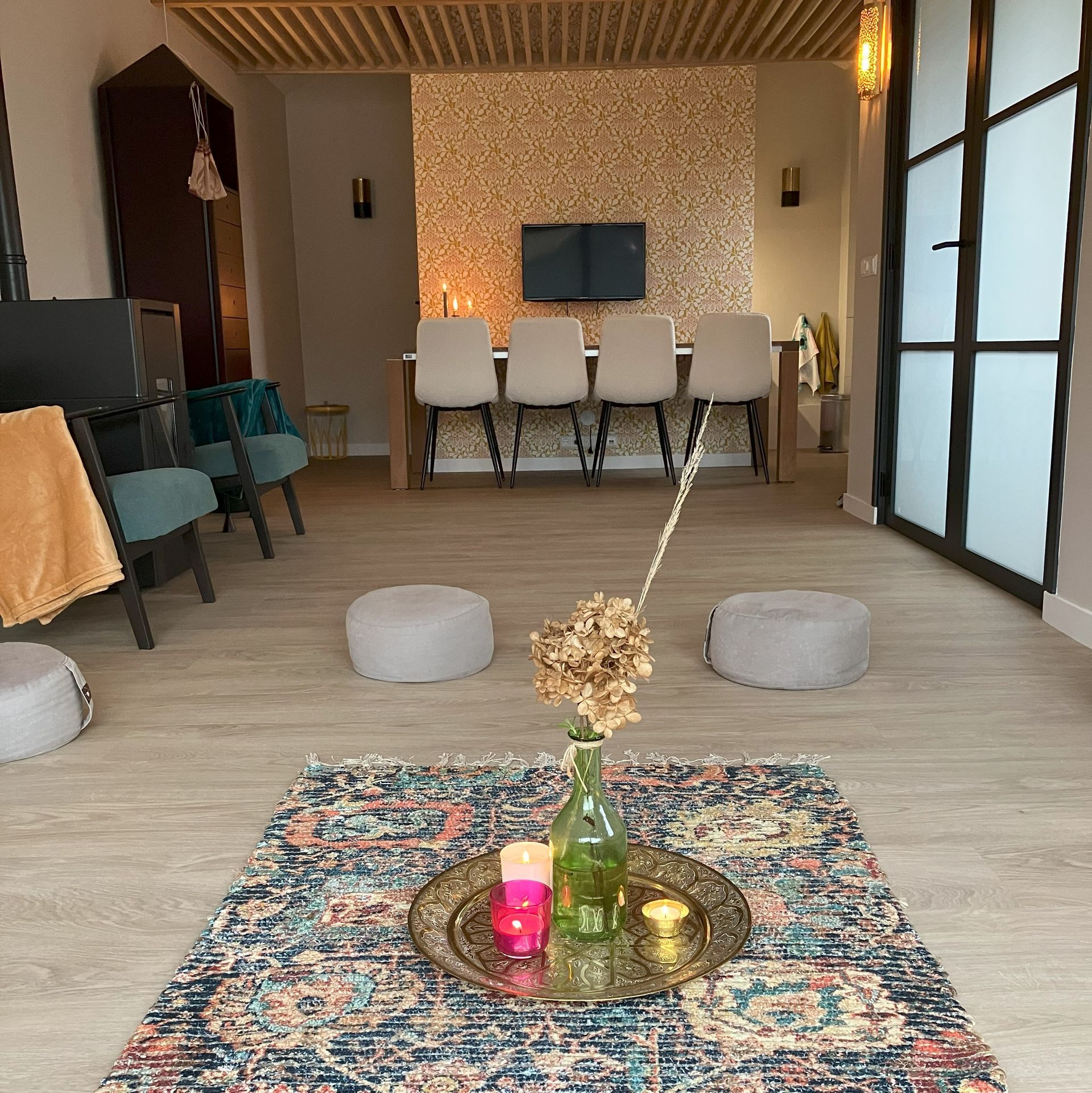 Praktijkruimte: tapijt, schaal met kaarsen, eettafel met stoelen, glazen deuren en accentmuur.